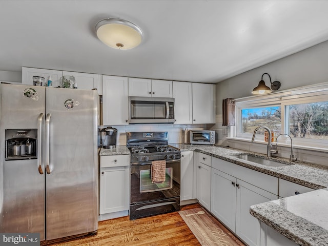 kitchen with sink, white cabinets, light hardwood / wood-style floors, stainless steel appliances, and light stone countertops