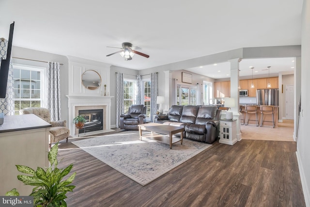 living room with dark hardwood / wood-style flooring, decorative columns, and ceiling fan