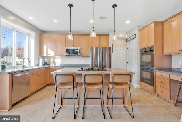 kitchen featuring stainless steel appliances, hanging light fixtures, a center island, and light brown cabinetry