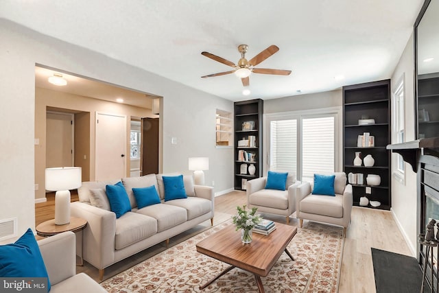 living room with ceiling fan, a fireplace, and light wood-type flooring