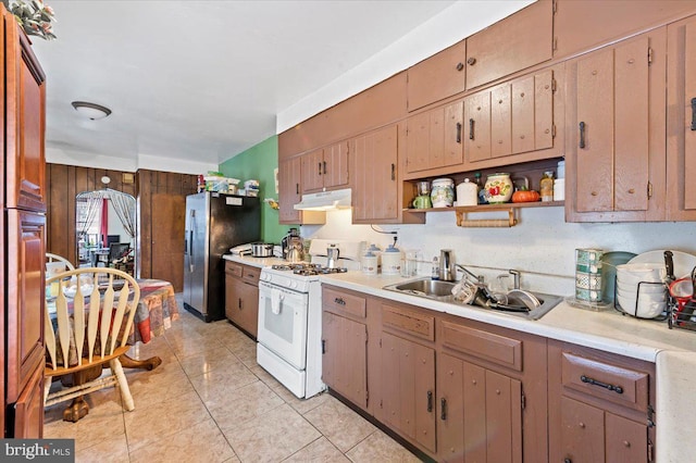 kitchen with wooden walls, sink, stainless steel fridge, light tile patterned floors, and gas range gas stove