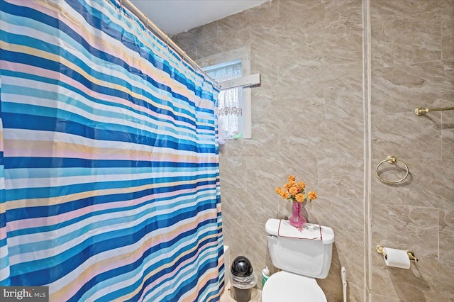 bathroom with walk in shower, toilet, and tile walls