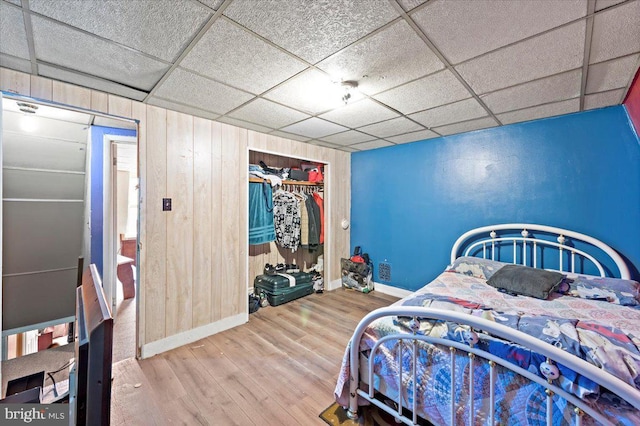 bedroom with a paneled ceiling, wood-type flooring, a closet, and wood walls