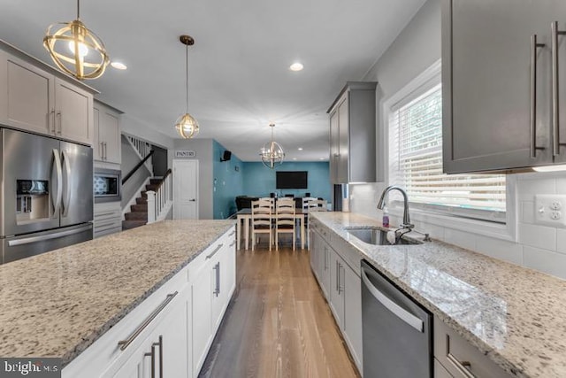 kitchen with sink, decorative light fixtures, appliances with stainless steel finishes, hardwood / wood-style floors, and backsplash