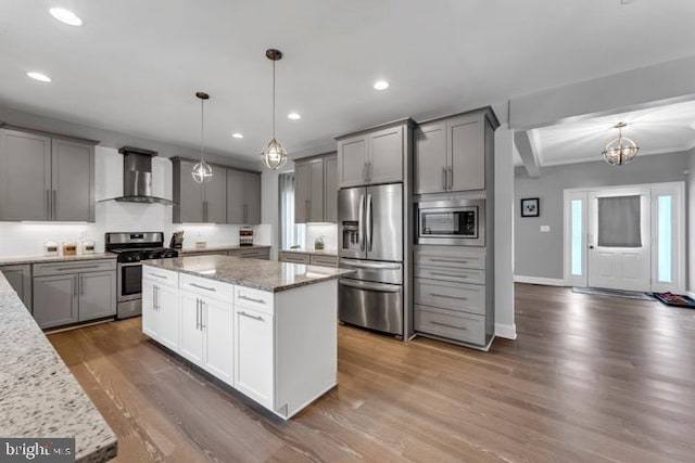 kitchen with wall chimney exhaust hood, light stone counters, a kitchen island, pendant lighting, and stainless steel appliances