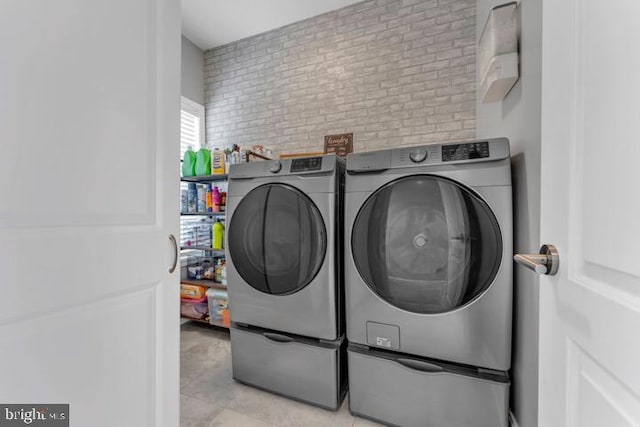 washroom with washing machine and dryer and brick wall