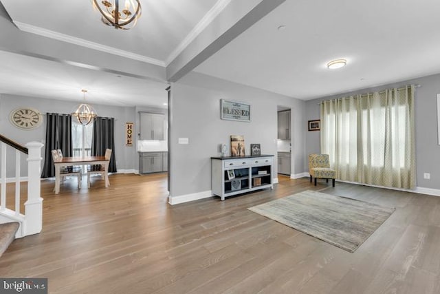 living area with a healthy amount of sunlight, hardwood / wood-style flooring, ornamental molding, and a chandelier