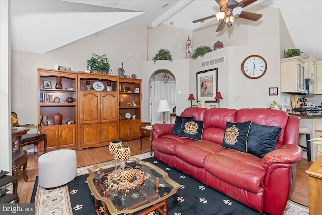 living room with beam ceiling, high vaulted ceiling, ceiling fan, and light wood-type flooring