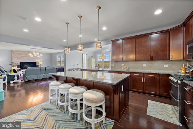 kitchen with hanging light fixtures, backsplash, stainless steel appliances, light stone counters, and a kitchen island