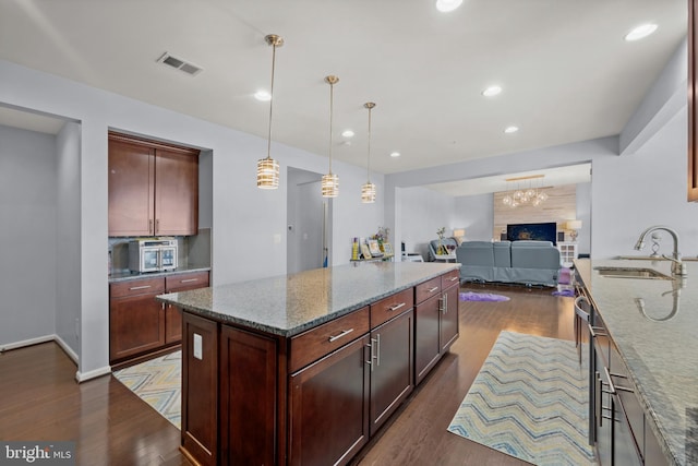 kitchen featuring pendant lighting, sink, dark wood-type flooring, a center island, and light stone countertops