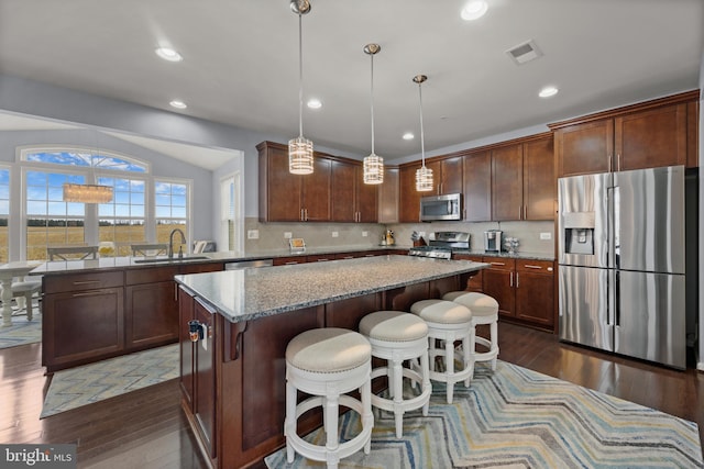 kitchen with pendant lighting, sink, stainless steel appliances, a center island, and dark hardwood / wood-style flooring