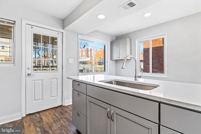 kitchen with light stone counters, gray cabinetry, a sink, visible vents, and dark wood-style floors