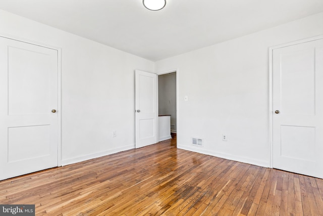 unfurnished bedroom featuring wood-type flooring, visible vents, and baseboards