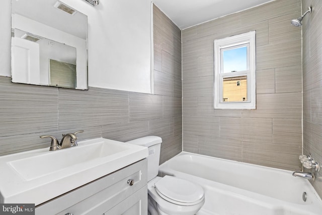 bathroom with tile walls, shower / bath combination, visible vents, toilet, and vanity