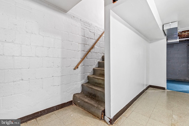 stairway with concrete block wall, baseboards, and tile patterned floors