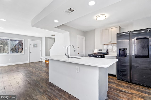 kitchen with dark wood finished floors, visible vents, appliances with stainless steel finishes, a sink, and an island with sink