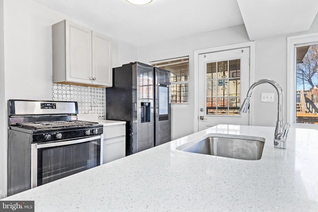 kitchen with stainless steel appliances, a sink, white cabinets, and light stone countertops