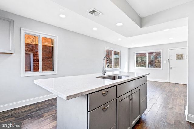 kitchen with dark wood finished floors, visible vents, gray cabinetry, a sink, and light stone countertops