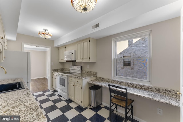 kitchen with sink, white appliances, built in desk, and cream cabinets