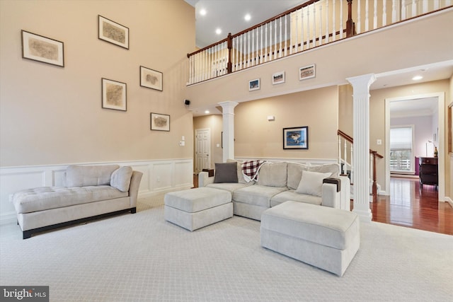 carpeted living room featuring a decorative wall, a wainscoted wall, recessed lighting, stairs, and ornate columns