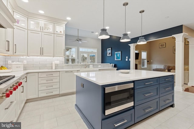 kitchen featuring stainless steel appliances, range hood, white cabinetry, and ornate columns