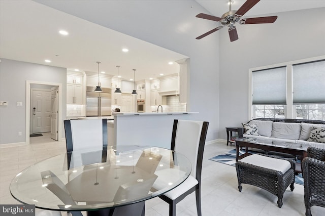 dining space with ceiling fan, light tile patterned floors, recessed lighting, a high ceiling, and baseboards