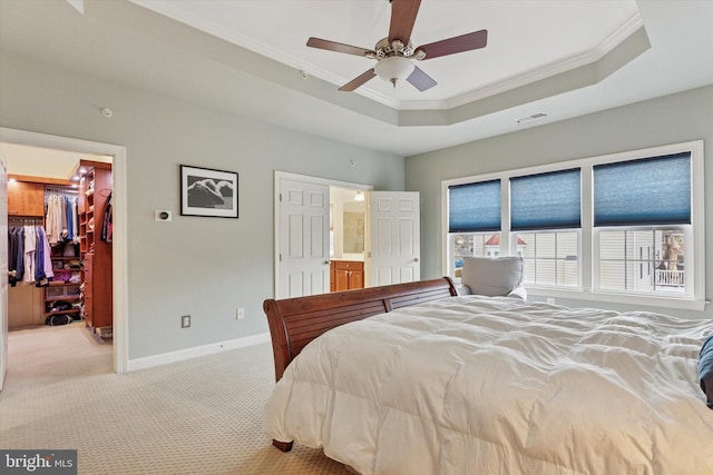 bedroom with a tray ceiling, a walk in closet, crown molding, light colored carpet, and visible vents