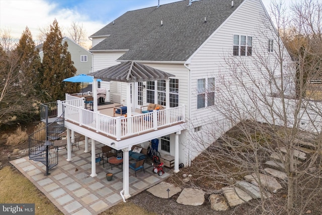 back of property with a shingled roof, outdoor dining space, a patio area, and a wooden deck