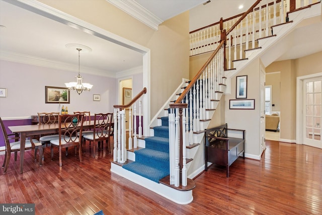 stairs with an inviting chandelier, wood-type flooring, ornamental molding, and baseboards