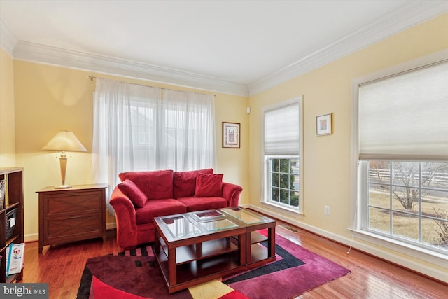 living area with baseboards, wood finished floors, visible vents, and crown molding