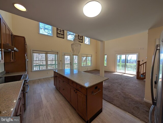 kitchen featuring a towering ceiling, stainless steel fridge, a center island, light stone countertops, and electric stove