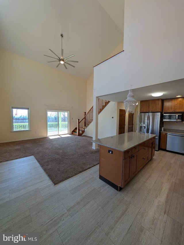 kitchen with a kitchen island, appliances with stainless steel finishes, high vaulted ceiling, decorative light fixtures, and light colored carpet