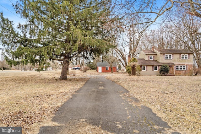 view of front of property featuring driveway, a chimney, and an outdoor structure