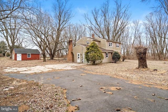 view of side of home with driveway, a chimney, and an outdoor structure