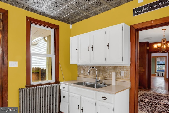 kitchen with sink, backsplash, radiator heating unit, plenty of natural light, and white cabinets