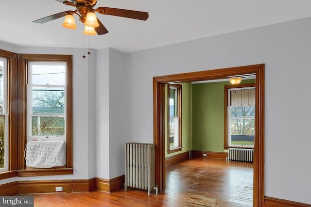 unfurnished room with ceiling fan, radiator, and light wood-type flooring