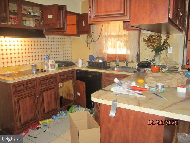 kitchen with light tile patterned floors, under cabinet range hood, a peninsula, a sink, and tasteful backsplash