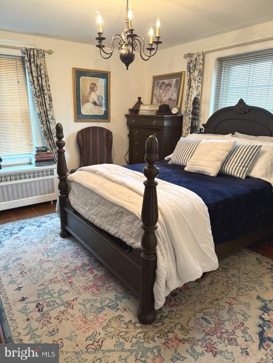 bedroom with an inviting chandelier, hardwood / wood-style flooring, and radiator heating unit