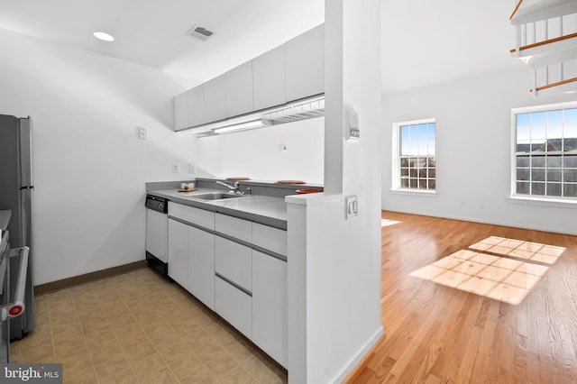 kitchen featuring visible vents, freestanding refrigerator, white dishwasher, a sink, and baseboards