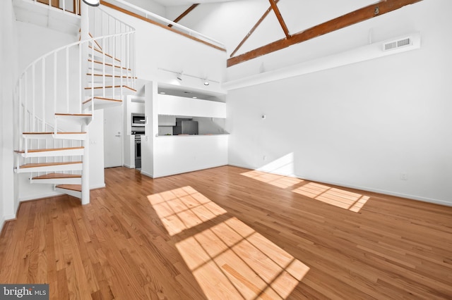 unfurnished living room featuring high vaulted ceiling, stairs, visible vents, and wood finished floors