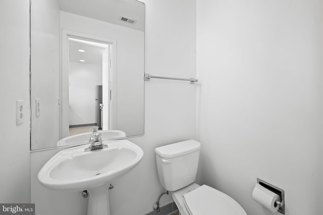 bathroom with toilet, a sink, and visible vents