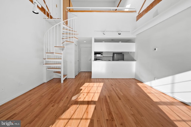 unfurnished living room with a high ceiling, wood finished floors, baseboards, stairs, and track lighting