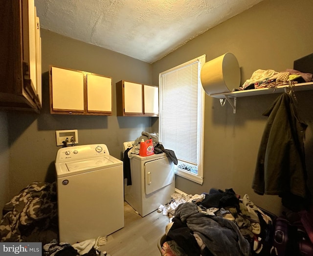 clothes washing area featuring a textured ceiling, light hardwood / wood-style flooring, cabinets, and washing machine and clothes dryer