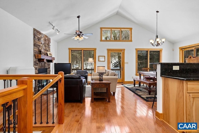 living room with ceiling fan with notable chandelier, a fireplace, high vaulted ceiling, and light wood-type flooring