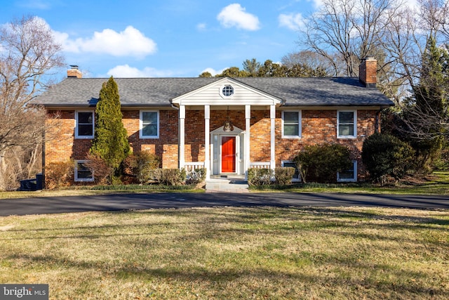 neoclassical / greek revival house with brick siding, a chimney, a front lawn, and aphalt driveway