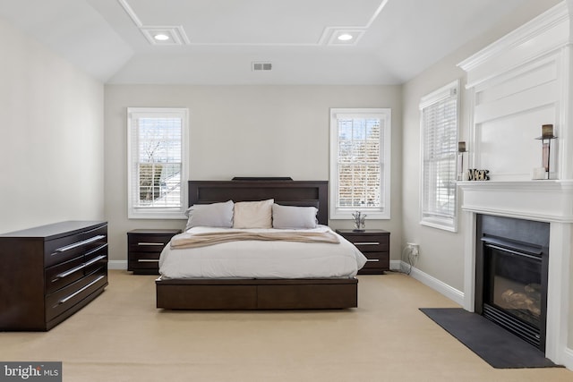 bedroom featuring visible vents, lofted ceiling, light carpet, multiple windows, and a glass covered fireplace