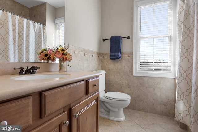 bathroom with tile patterned flooring, tile walls, toilet, wainscoting, and vanity