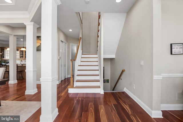 stairs with decorative columns and wood finished floors