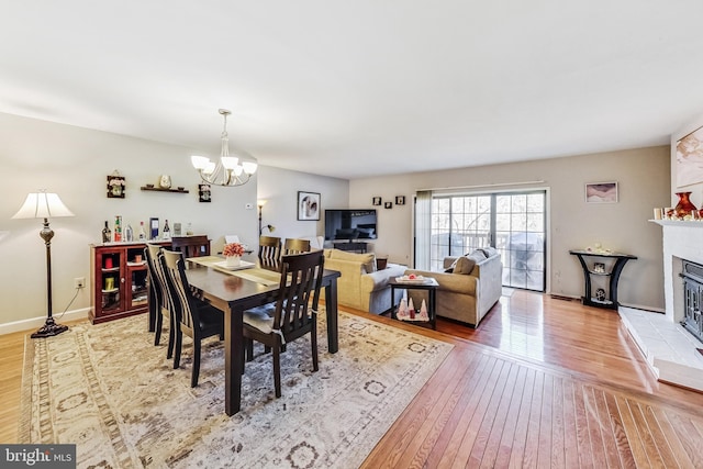 dining area featuring a chandelier, a glass covered fireplace, baseboards, and wood finished floors