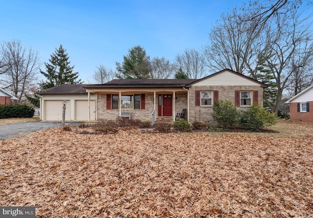 ranch-style home with aphalt driveway, brick siding, covered porch, an attached garage, and crawl space